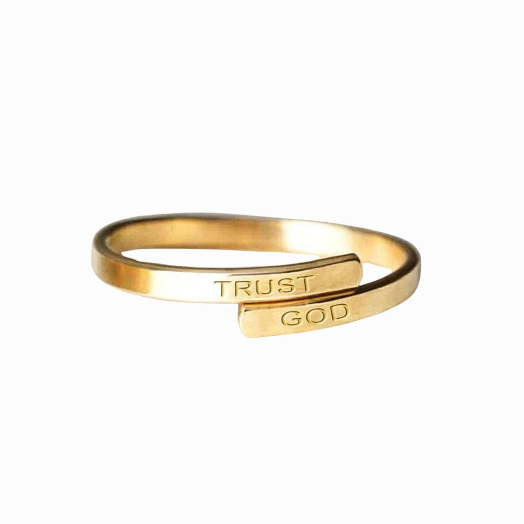 Gold ring with 'TRUST GOD' engraving on a white background