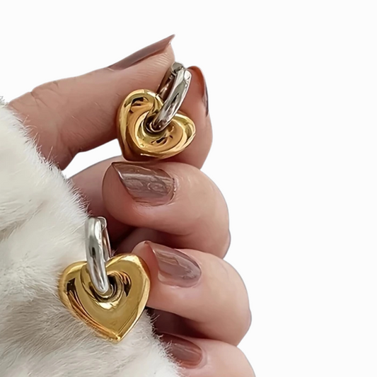 Gold and silver heart-shaped charms held between fingers against a white background