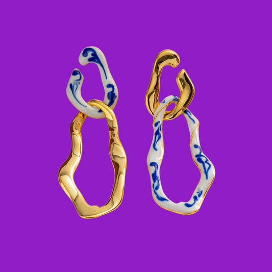 Gold and blue patterned earrings on a purple background