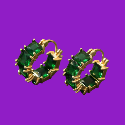 Gold hoop earrings with green gemstones on a purple background