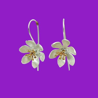 Silver flower-shaped earrings with gold accents on a purple background