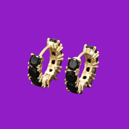 Gold hoop earrings with black gemstones on a purple background
