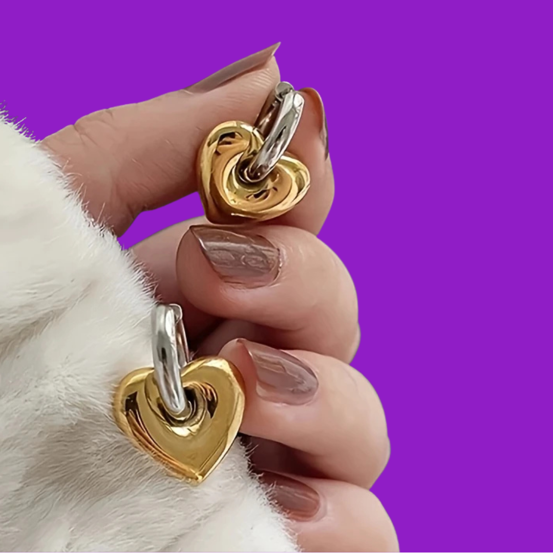 Gold and silver heart-shaped earrings held by a hand against a purple background