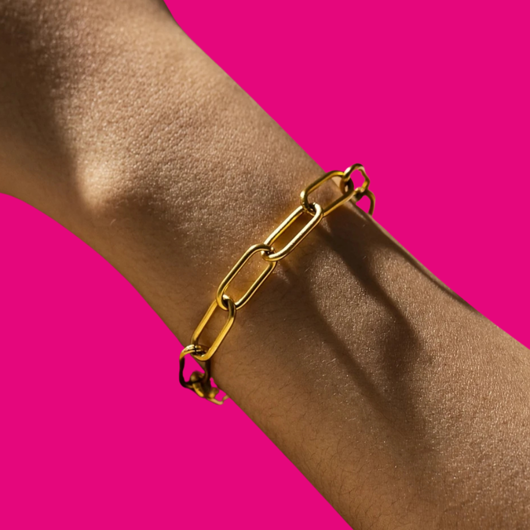 Gold chain bracelet on a wrist against a pink background
