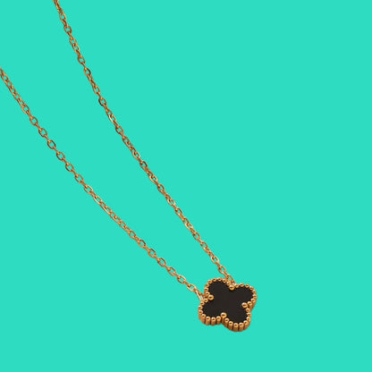 Gold necklace with a clover-shaped pendant on a teal background