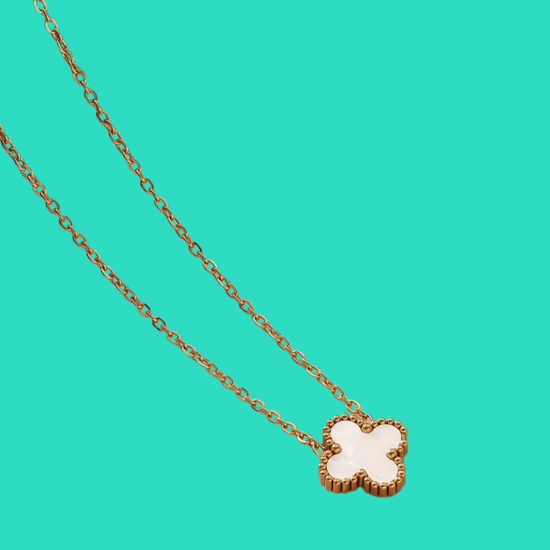 Gold necklace with a clover-shaped pendant on a teal background