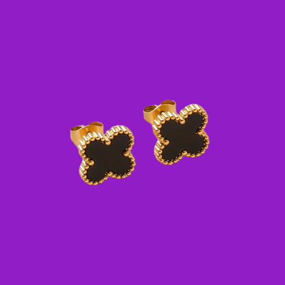 Gold and black clover-shaped earrings on a purple background