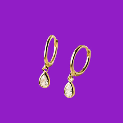 Gold hoop earrings with teardrop-shaped charms on a purple background
