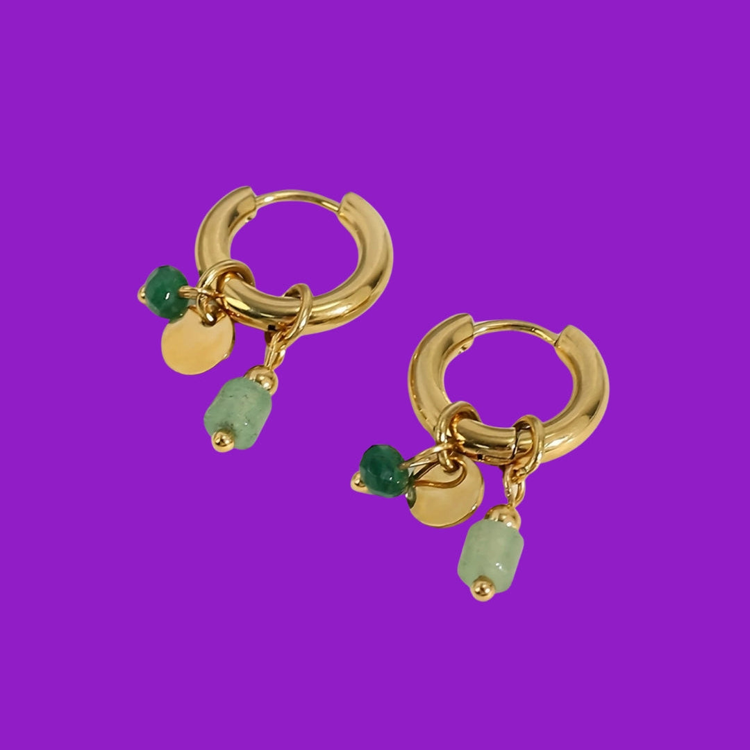 Gold hoop earrings with green beads on a purple background