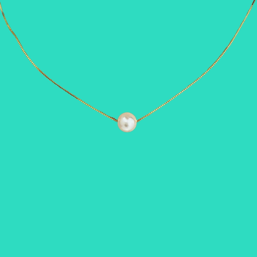 Gold necklace with a single pearl pendant on a teal background
