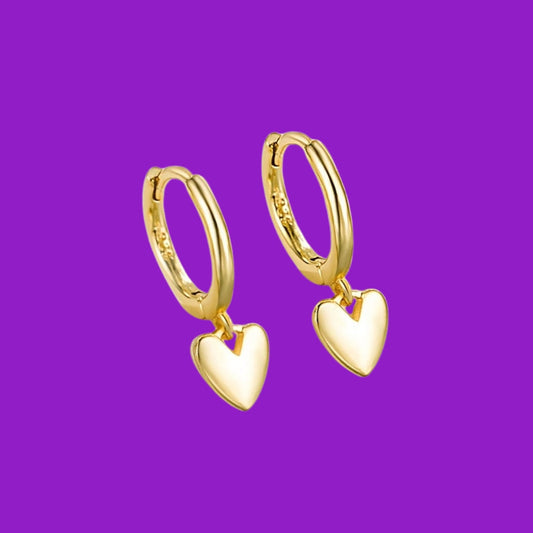 Gold hoop earrings with heart pendants on a purple background