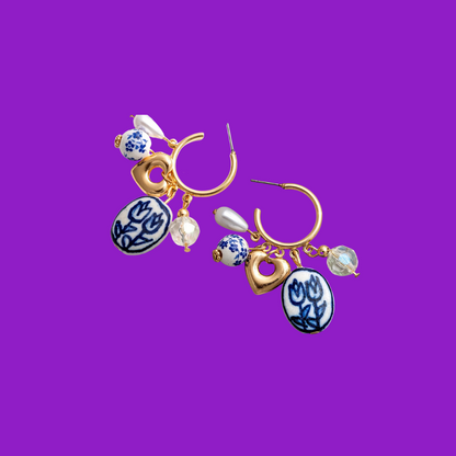 Gold hoop earrings with blue and white ceramic charms on a purple background