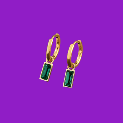 Gold hoop earrings with green gemstones on a purple background
