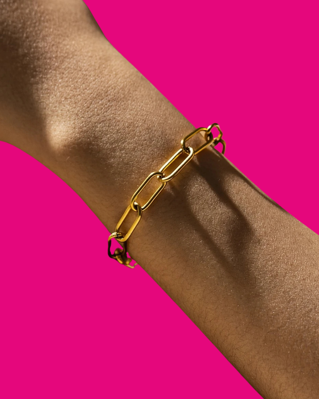 Gold chain bracelet on a wrist against a pink background
