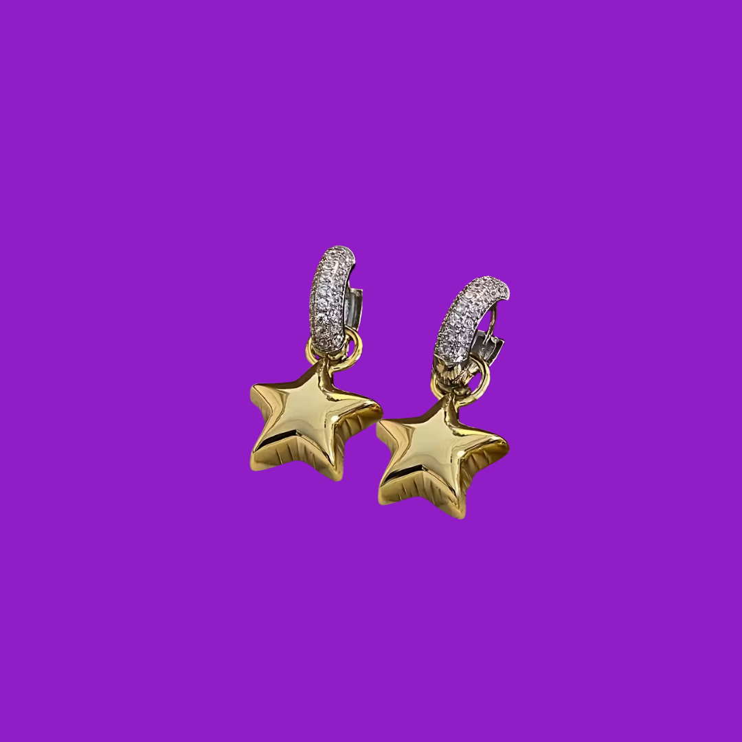 Gold star-shaped earrings with clear stones on a purple background