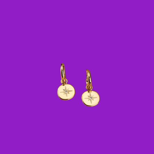 Gold earrings with star designs on a purple background