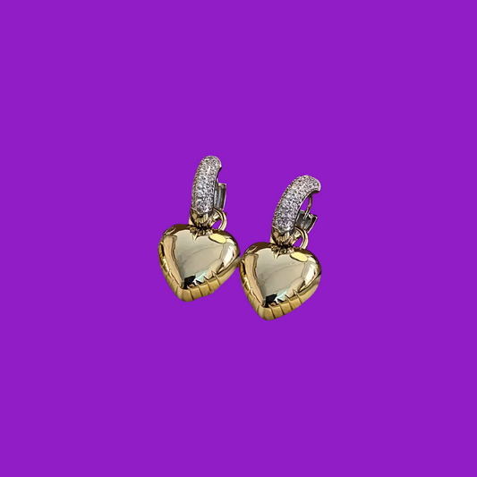 Gold heart-shaped earrings with clear stones on a purple background