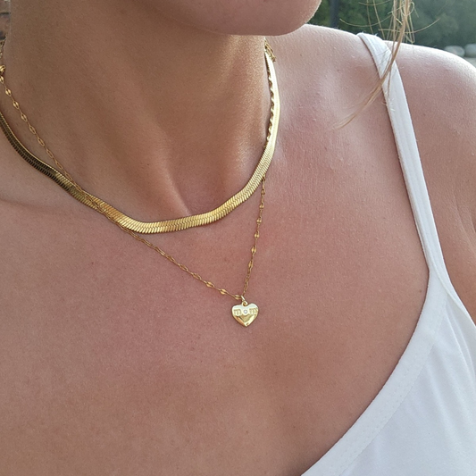 Close-up of a person wearing a gold necklace with a heart pendant.