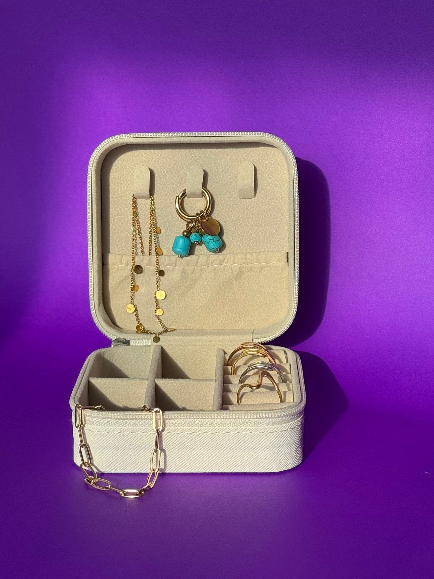 Open beige jewelry case with gold necklaces and earrings on a purple background