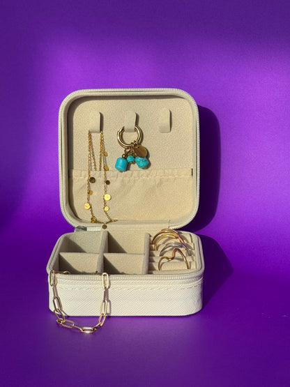 Open beige jewelry case with gold necklaces and earrings on a purple background