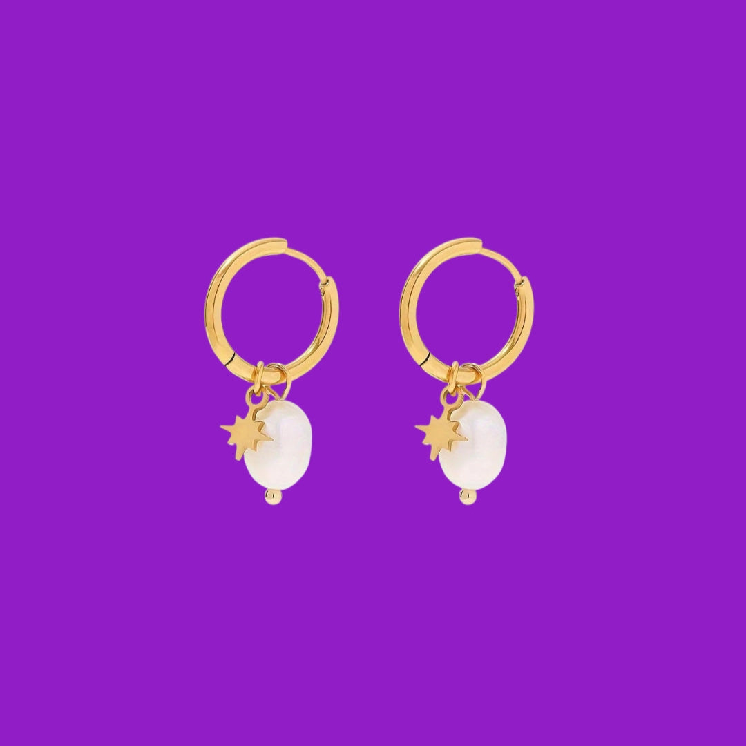 Gold hoop earrings with white stones and star charms on a purple background