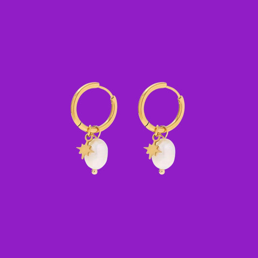 Gold hoop earrings with white stones and star charms on a purple background